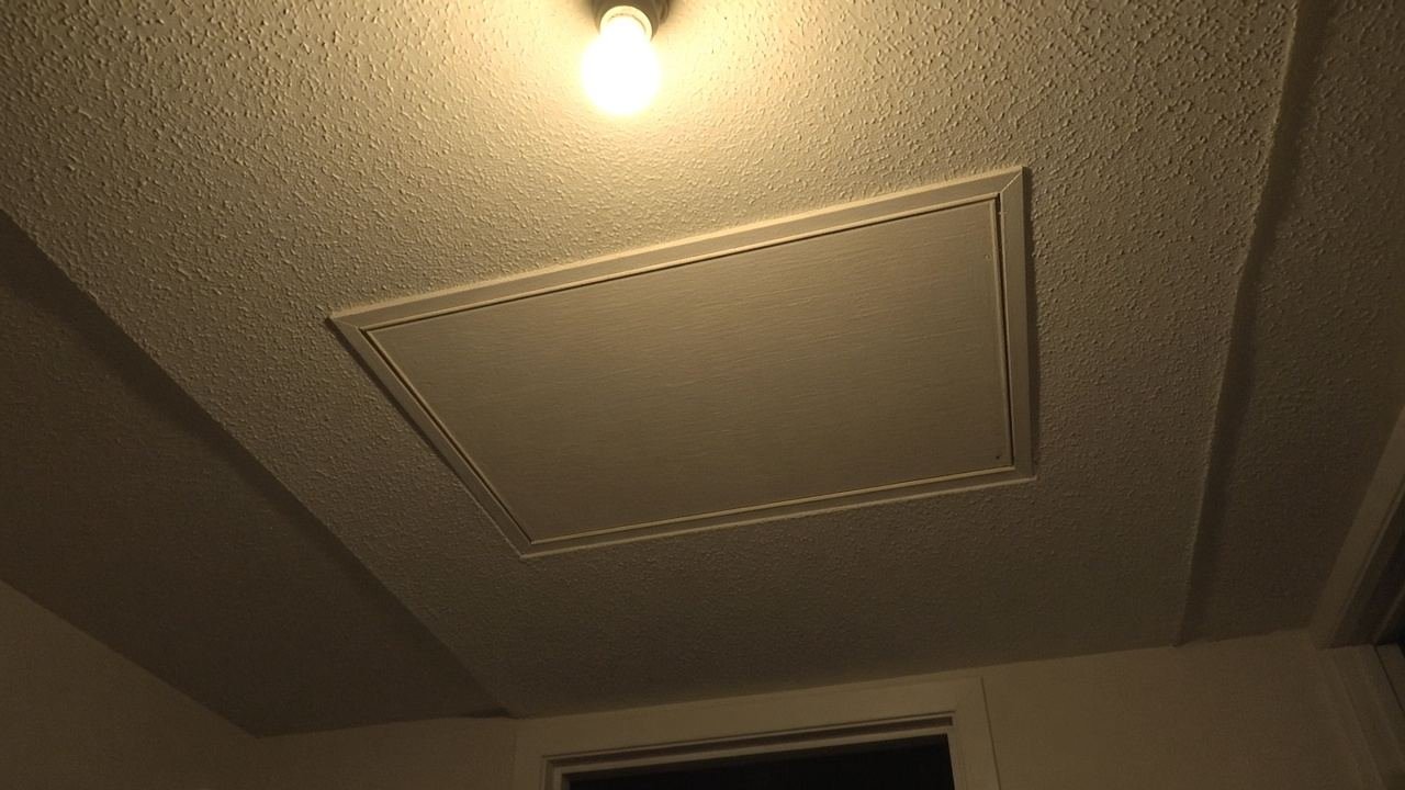 A closed attic hatch in a Florida hallway ceiling