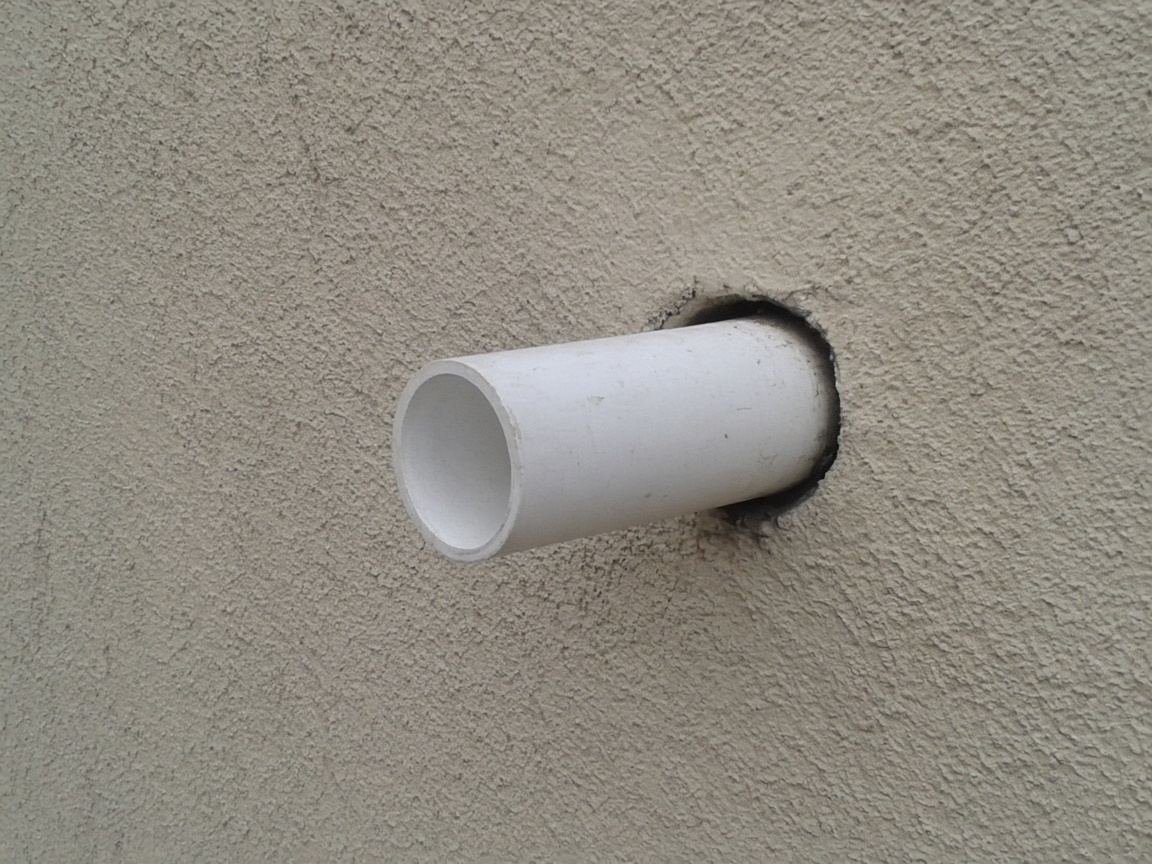 Dark gap around a pipe where it enters a stucco wall